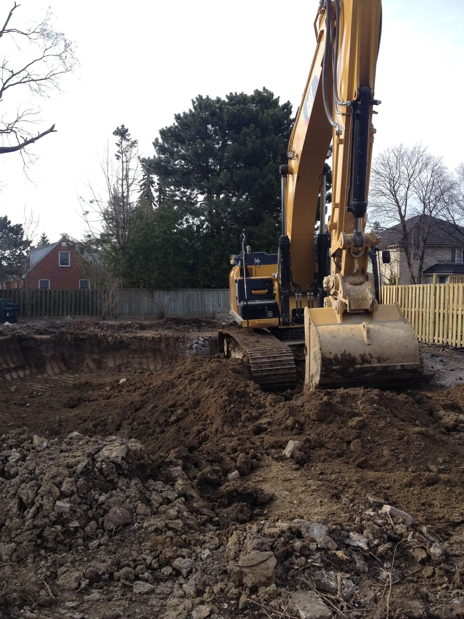An excavator at the edge of the dug-out lot, with the soil turned over where the house will stand.