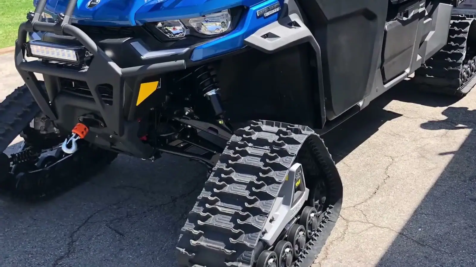 A blue Can-Am Defender UTV on rear tracks in a driveway.