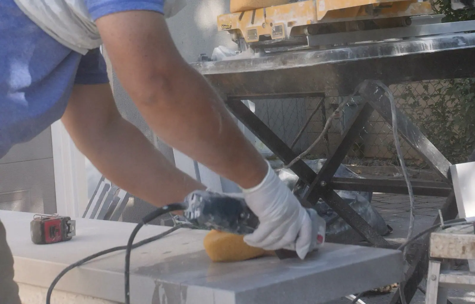 A gloved hand holding a grinder against the edge of a pale slab on a cutting bench.