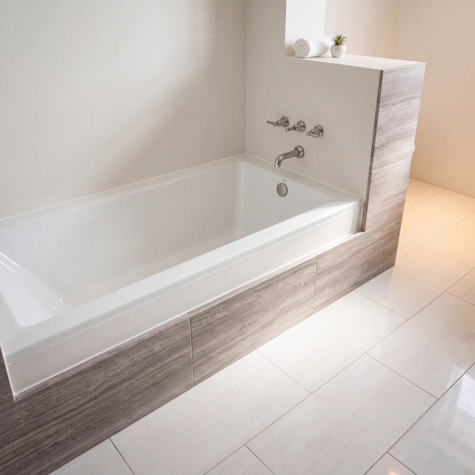 A white built-in bathtub with a wood-grain tile surround and a wall-mounted tub filler, on a pale tile floor, with a tiled half wall behind it.