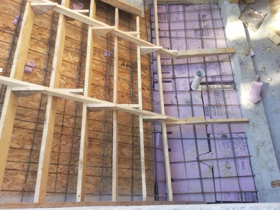Stair formwork of boards and joists with steel reinforcing bars, and pink rigid insulation with rebar mesh beside it.