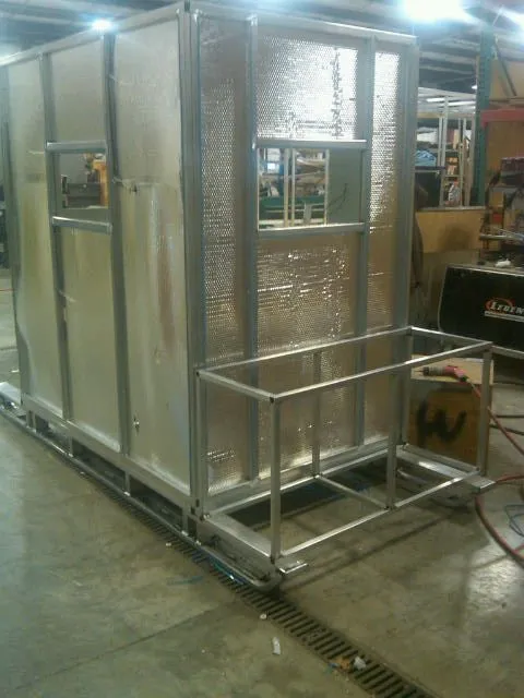 An aluminium-frame ice hut shell on a base frame in a shop, with silver foil insulation.