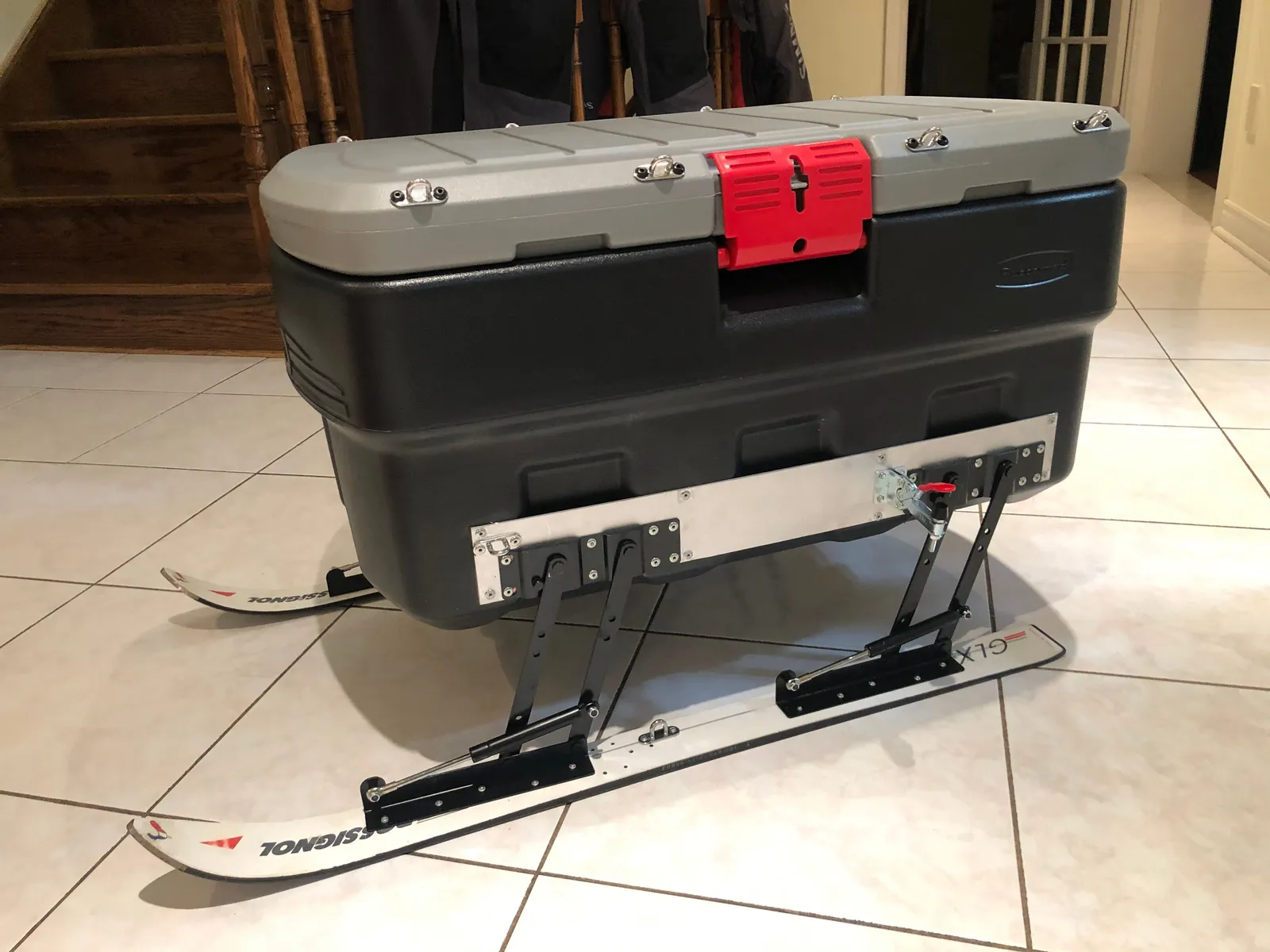 A large grey tub mounted on ski runners, on a tile floor.
