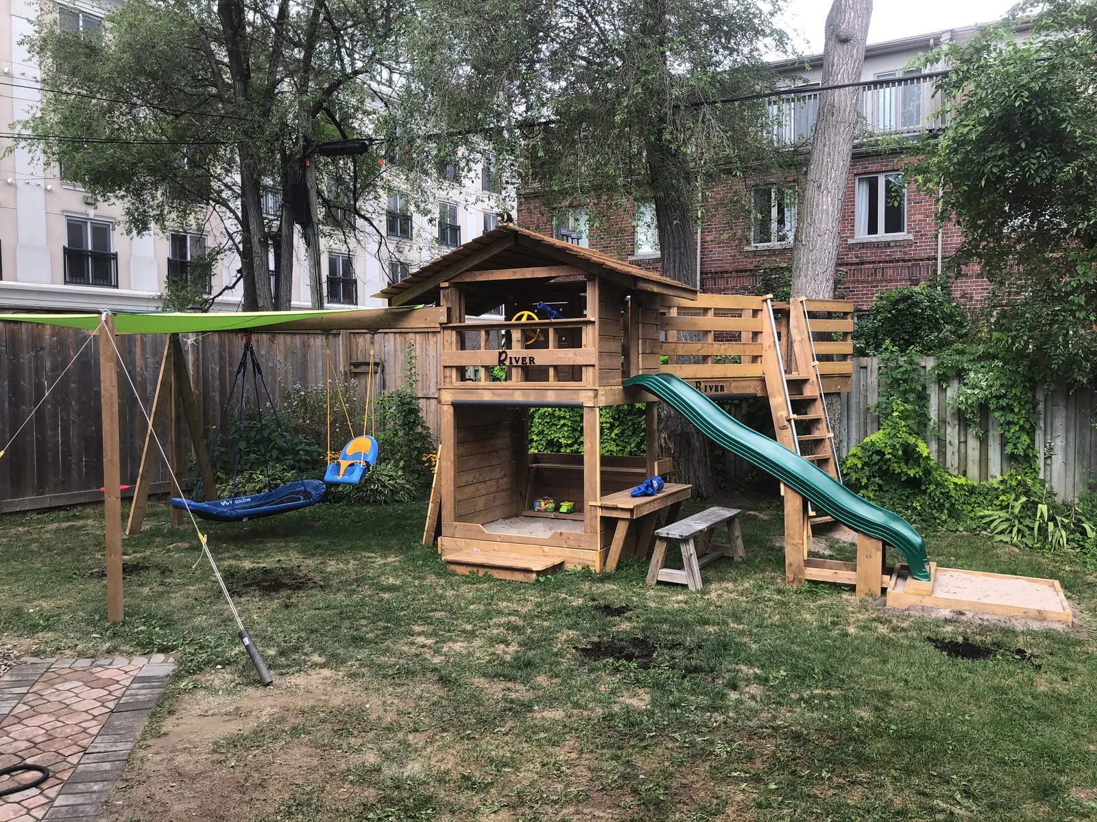 A wide view of the play fort, slide and swing set in a backyard.