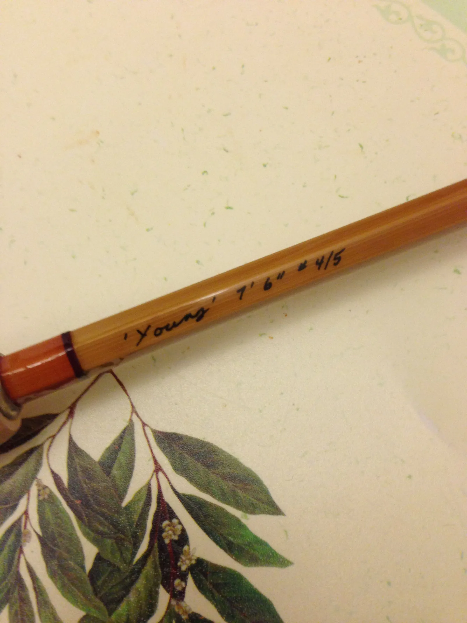 A split-cane rod laid across a leaf print.