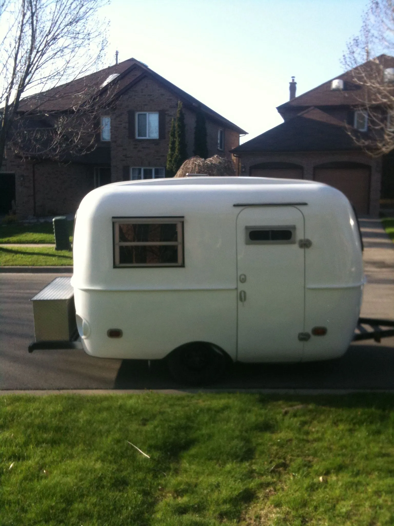 A small white vintage camper trailer parked outside a house.