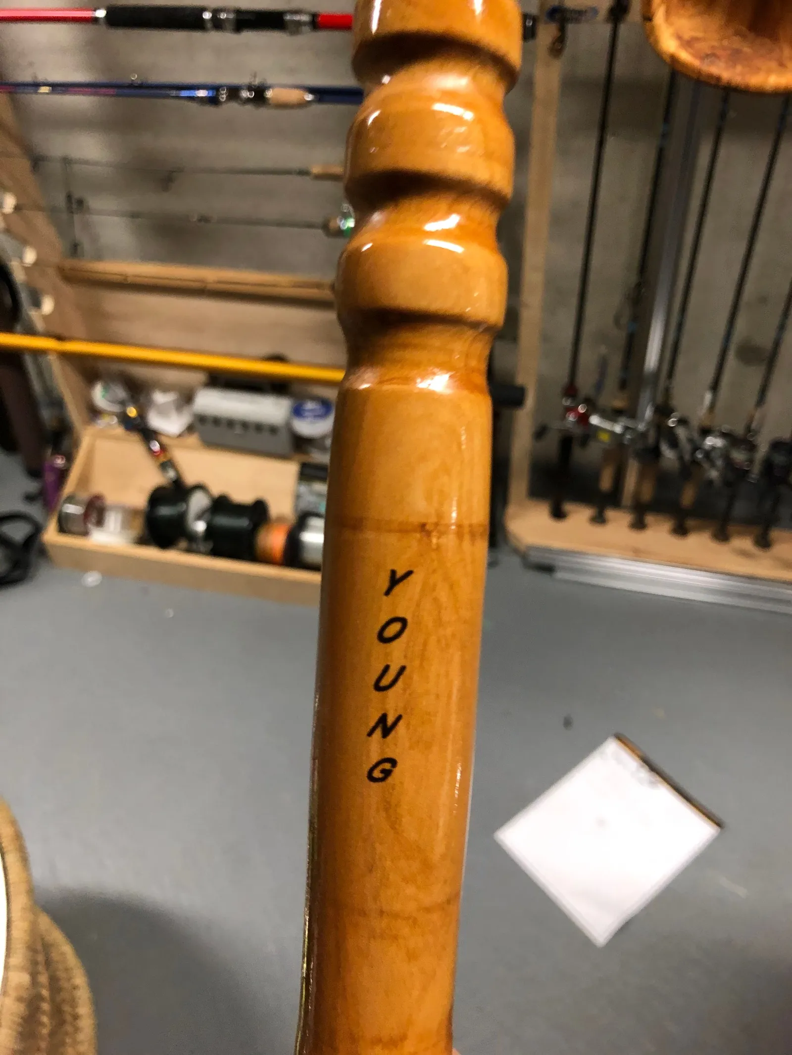 A turned wooden handle with engraved lettering, with a rod rack behind it.